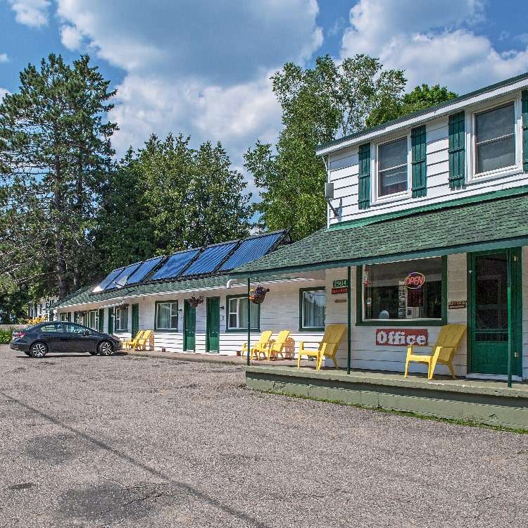The front of the East Gate Motel showing the office of Algonquin Accommodations and doors to individual motel rooms with pine trees behind the motel.
