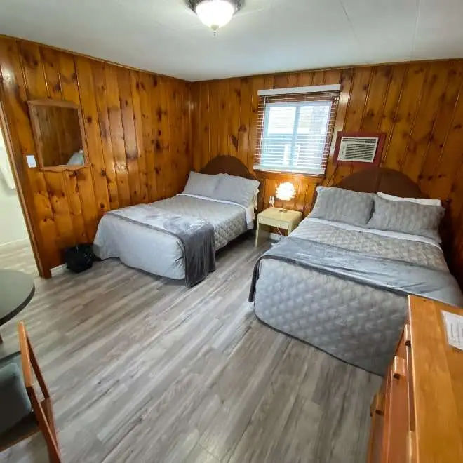 A newly renovated room at Rolling Rapids Motel showing two beds, cottage style wooden walls and sunlight coming through a window.