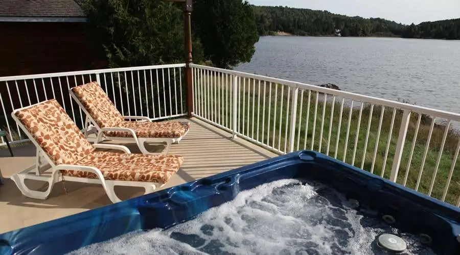 A balcony with two lounge chairs and a hot tub overlooking a lake at Couples Resort a hotel near Algonquin Park