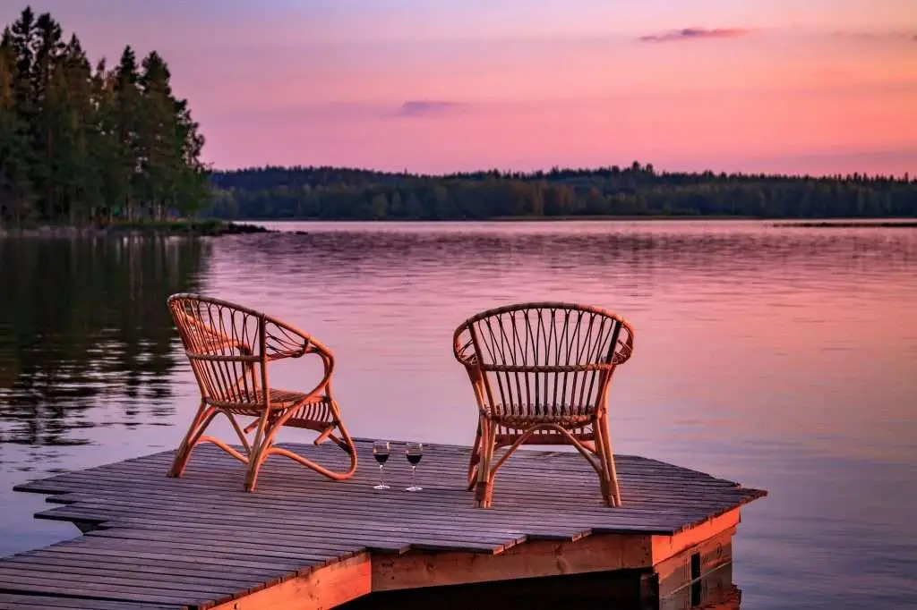 Two wooden chairs on a wood dock overlooking a lake at sunset