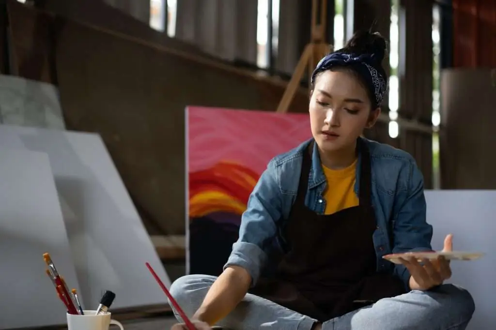 Asian Female Artist Draws create art piece with palette and brush painting at studio.