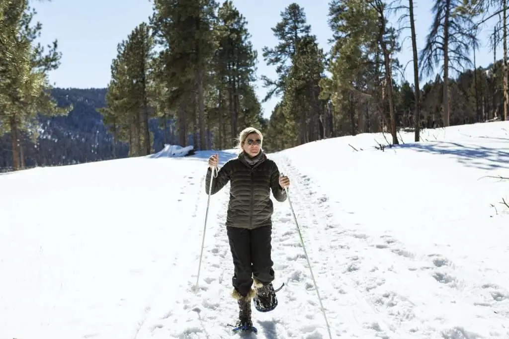 Adult woman wearing snow shoes with poles on a trail.