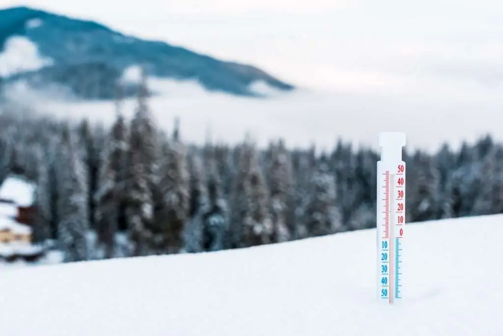 thermometer in snowy mountains with pine trees and white fluffy clouds