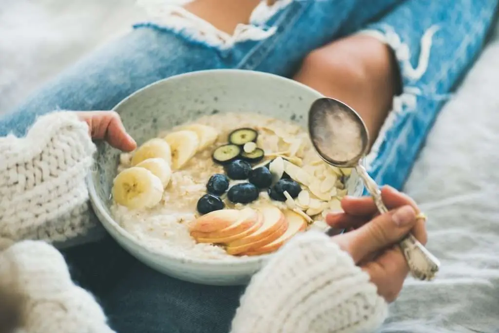 Woman in jeans and sweater eating healthy oatmeal porriage