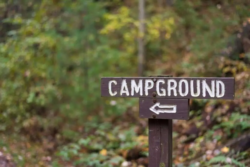 Closeup of a wooden campground sign with arrow along hiking trail