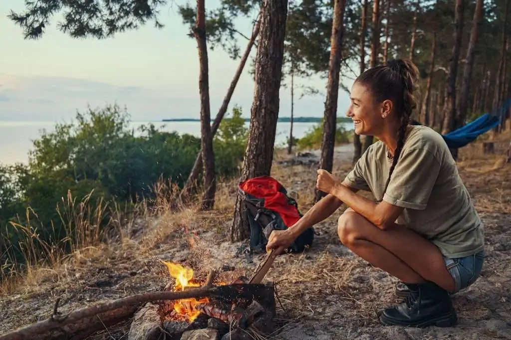 Happy traveller is adding firewood to campfire