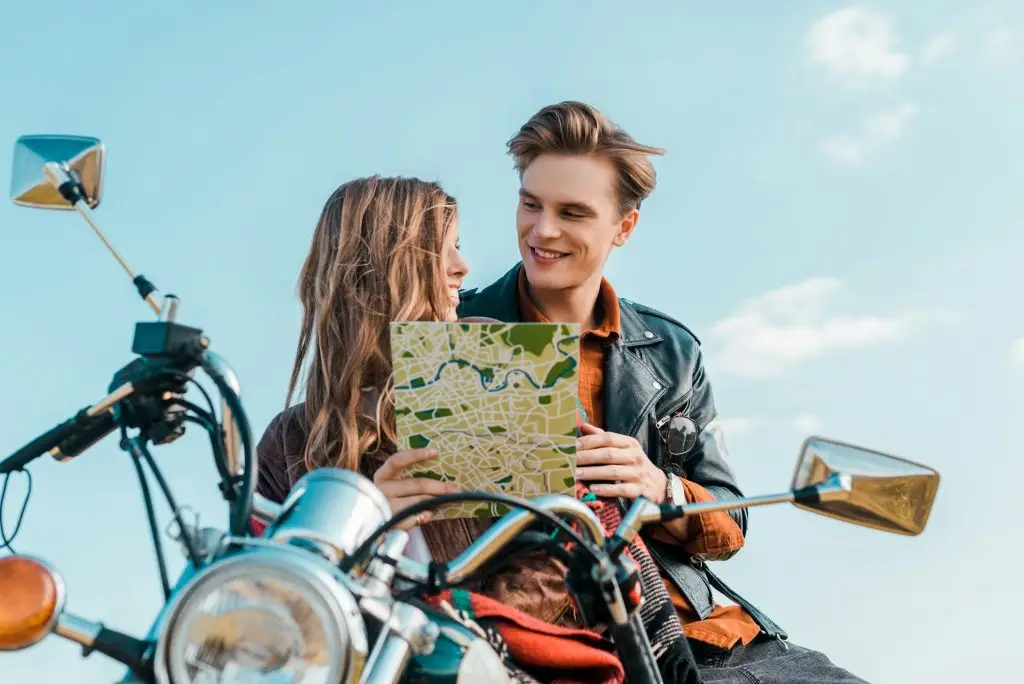 young couple of travelers holding map and sitting on motorbike against blue sky