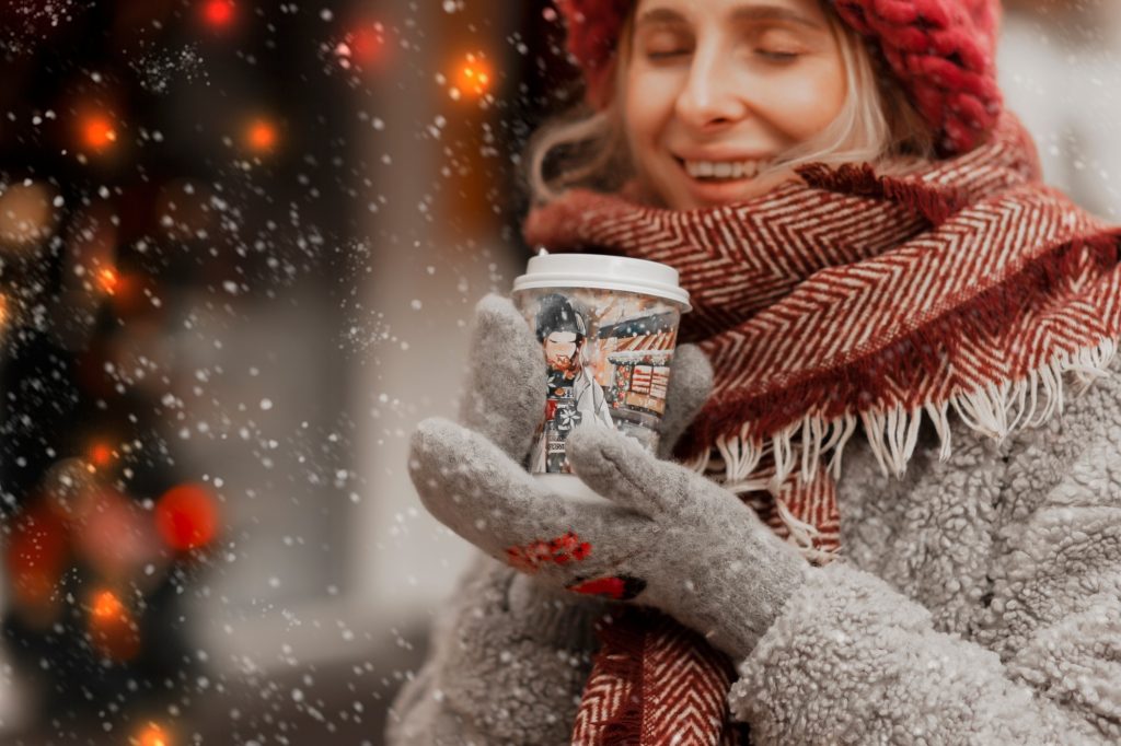 happy girl in a knitted hat drinks coffee and enjoys winter and snow