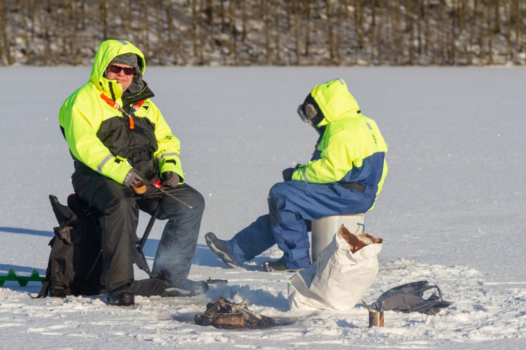 Two men ice fishing on the frozen winter lake, warm lined overalls, fireplace on the ice, outdoor