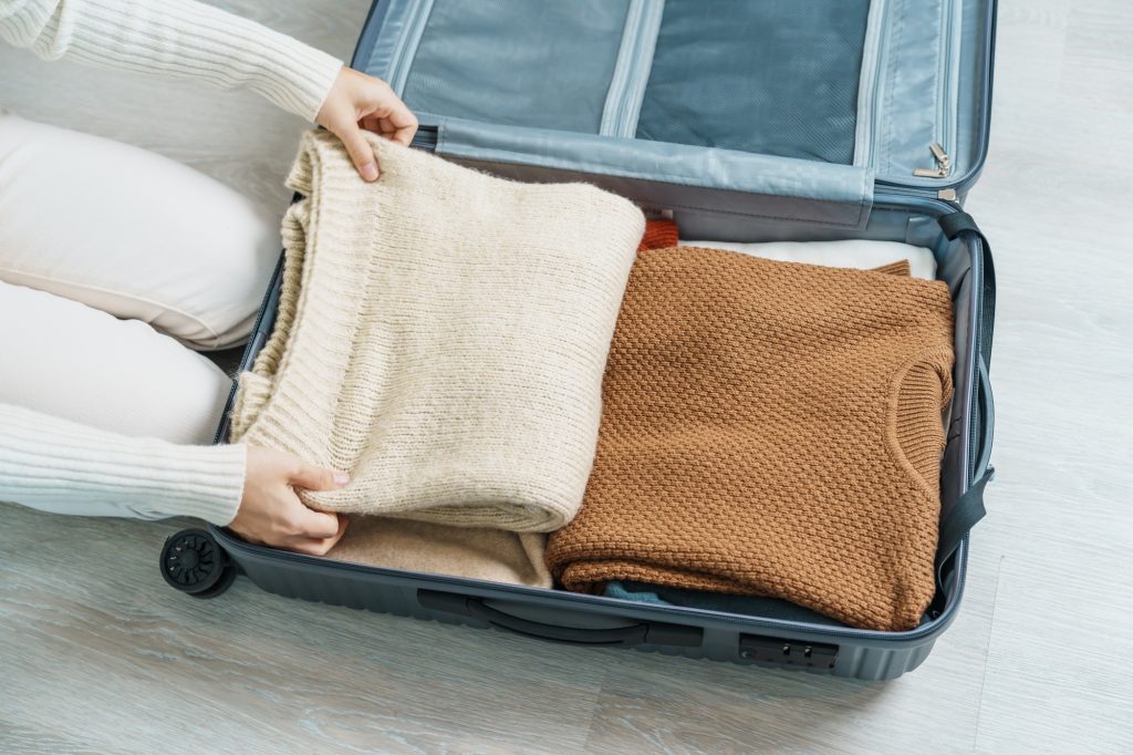 Woman hand packing her winter clothes in luggage.